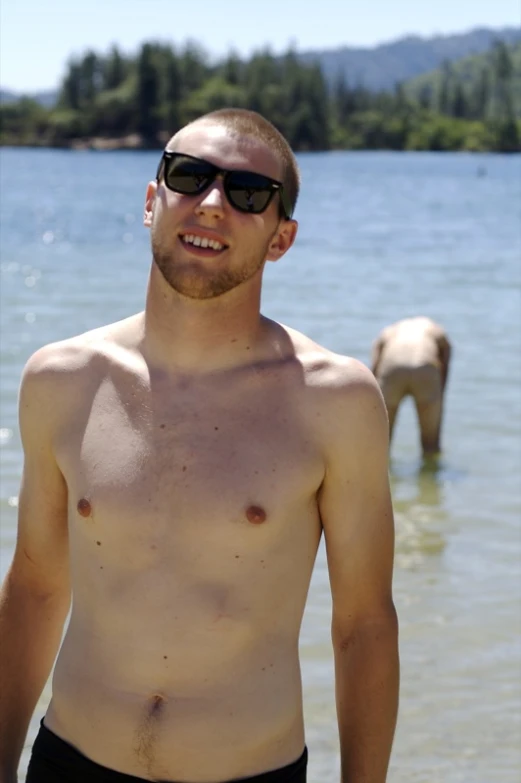 shirtless man standing in the water with horse behind