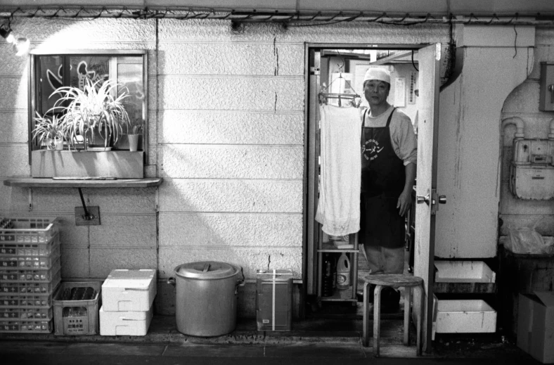 man with apron standing in doorway between refrigerators