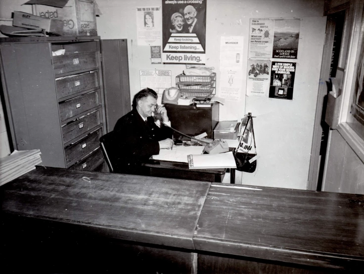 a man sitting in front of a desk on his cellphone