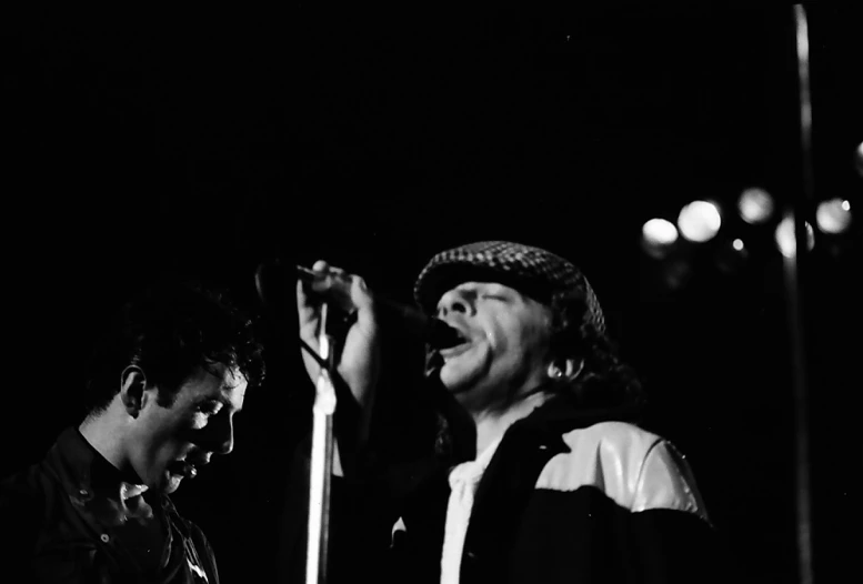 two young men stand at a microphone together