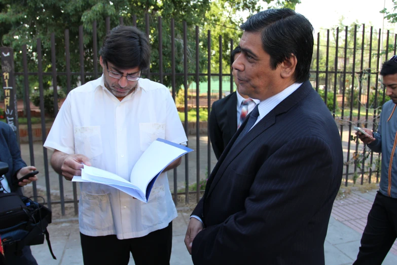 two men are in front of a fence and holding an open book