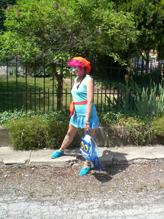 woman with large sunglasses, blue dress and bright orange hat walking down the sidewalk