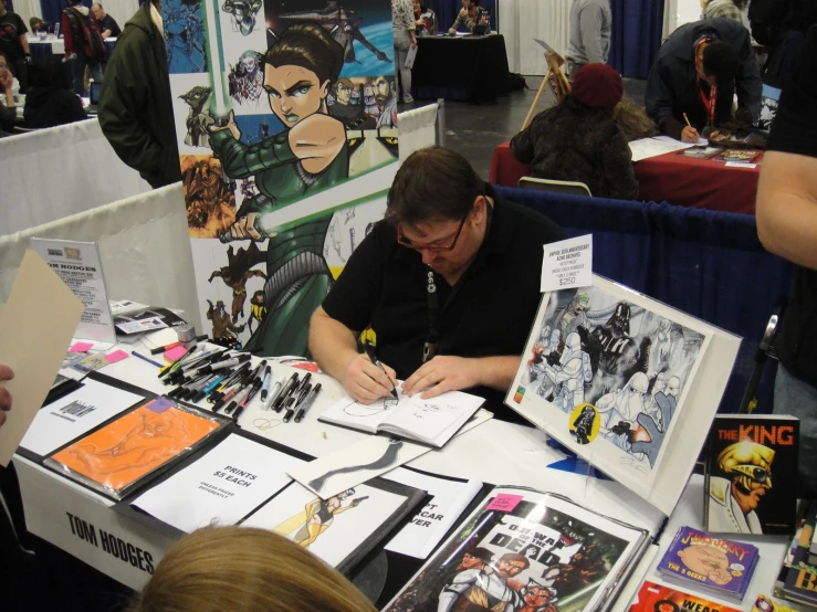 a man signing a book with comic posters on it