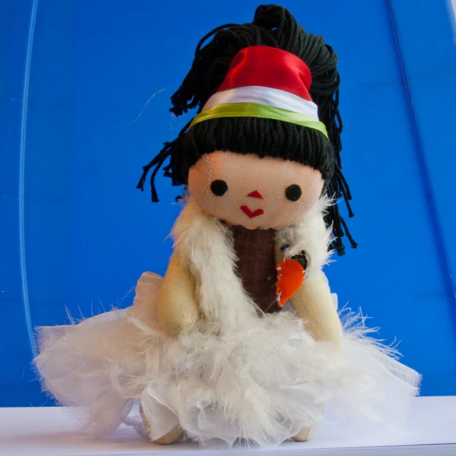 the doll with a dress and hat sits in front of a blue background