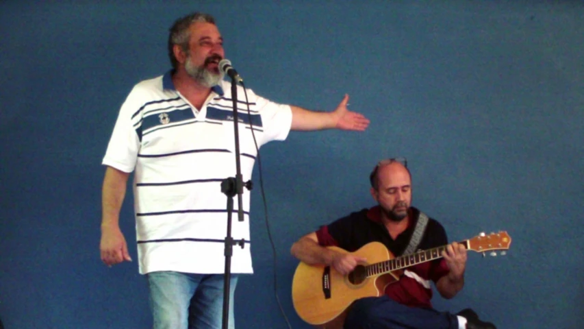 a man holding an acoustic guitar and another person standing behind him