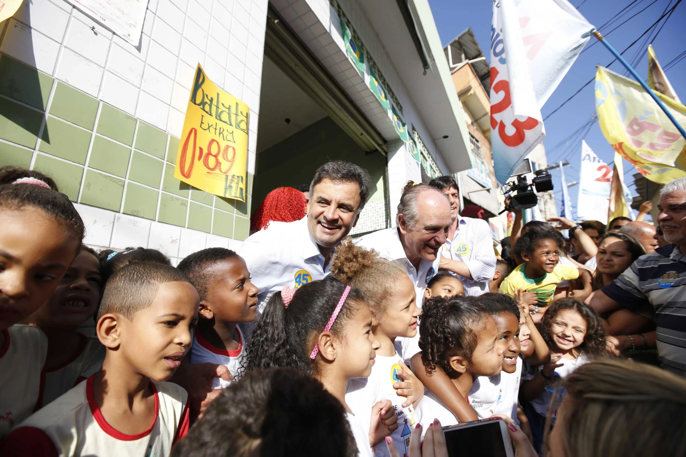 man in white shirt surrounded by children in front of building