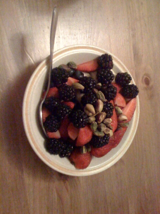 a bowl filled with berries and blackberries, next to a fork