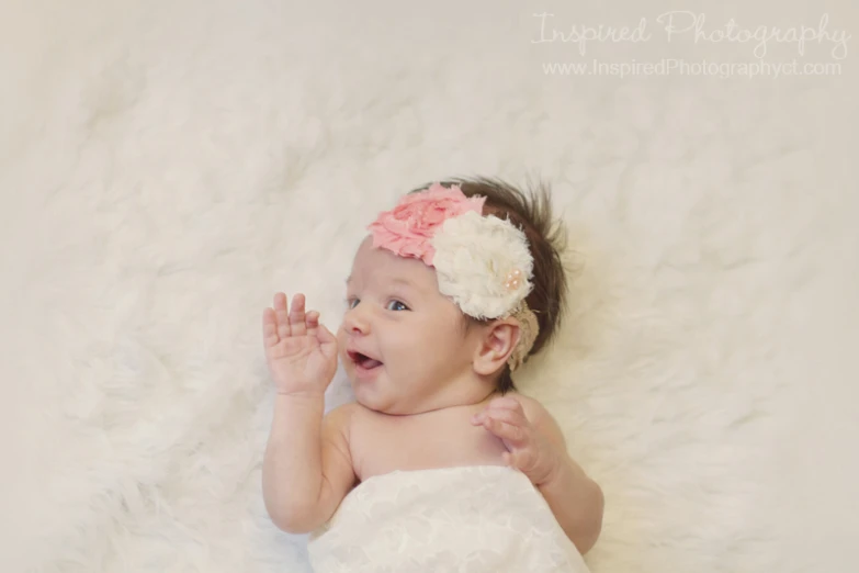 baby girl with a flower in her hair is lying on a fluffy blanket