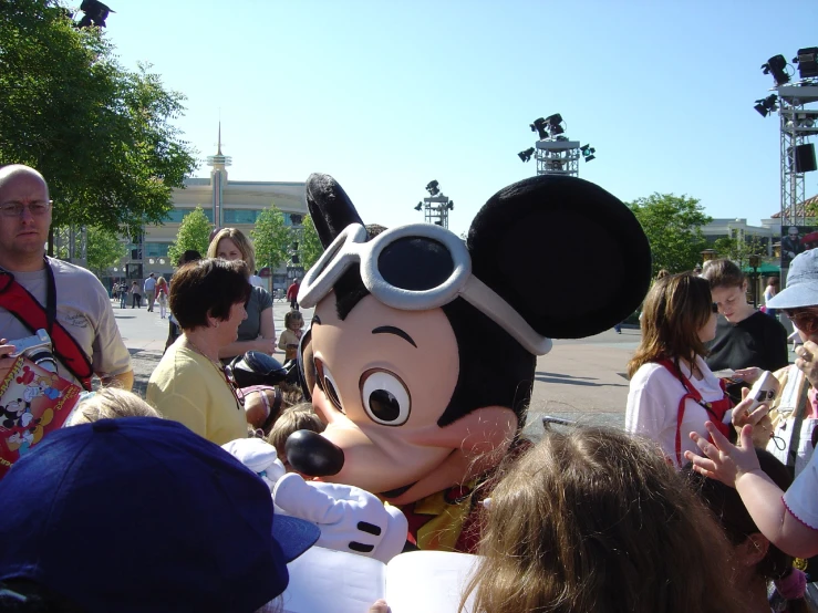 a mouse mascot dressed in sunglasses with many people around him