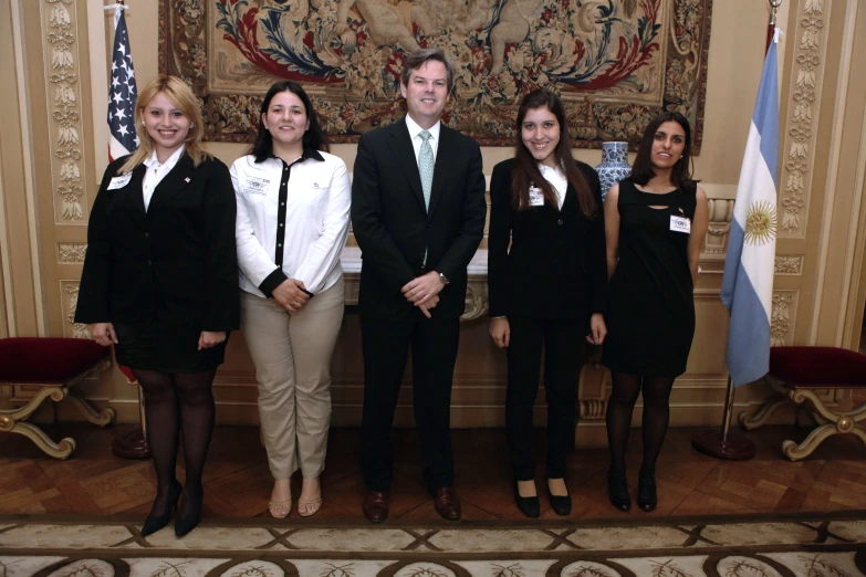 six people posing in formal attire next to two flags