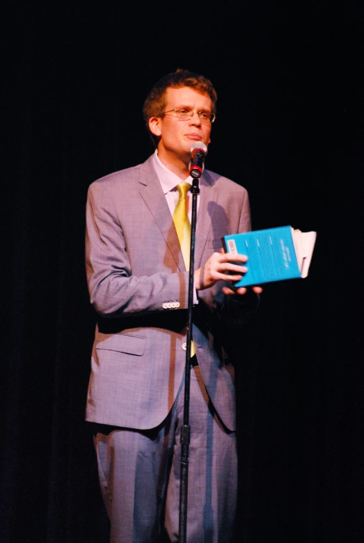 a man holding up a blue book standing in front of a microphone