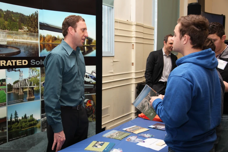 there is a man standing near a poster talking to another man