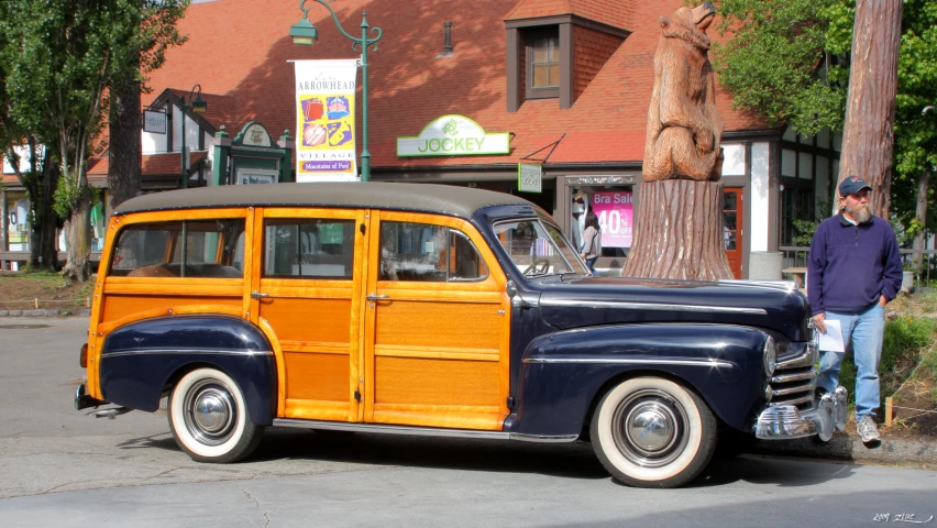 an old, brown and tan woody car is parked by a tree in front of the store