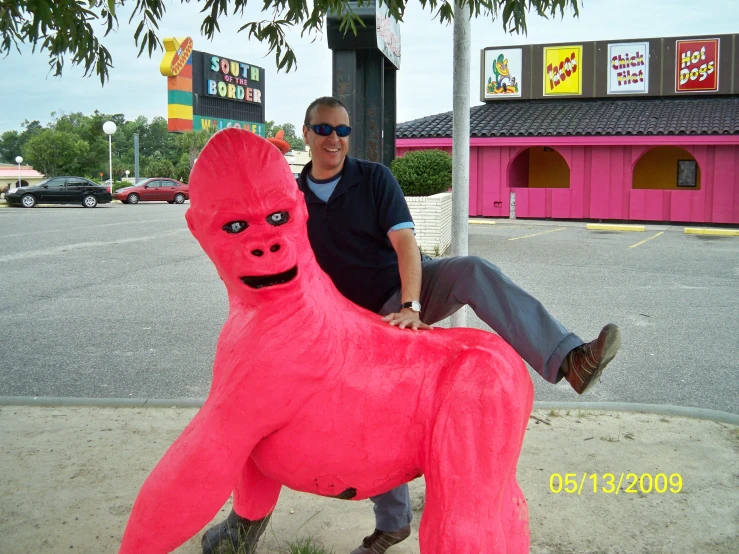 a man in black shirt and sunglasses posing for a po next to a giant pink object