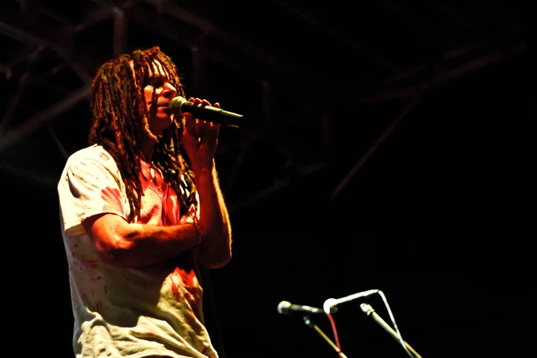 man with dread locks speaking on stage in dark