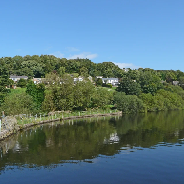 a blue sky and a green hillside line the shore of a lake