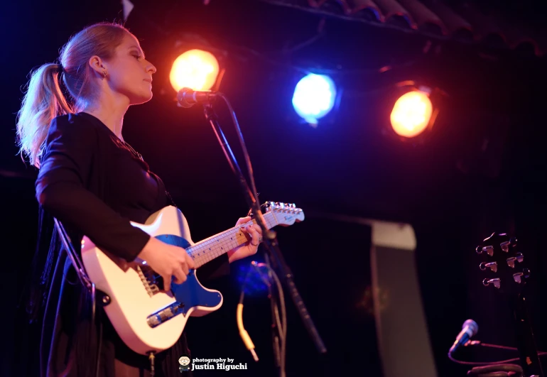 woman singing into microphone and playing guitar at concert