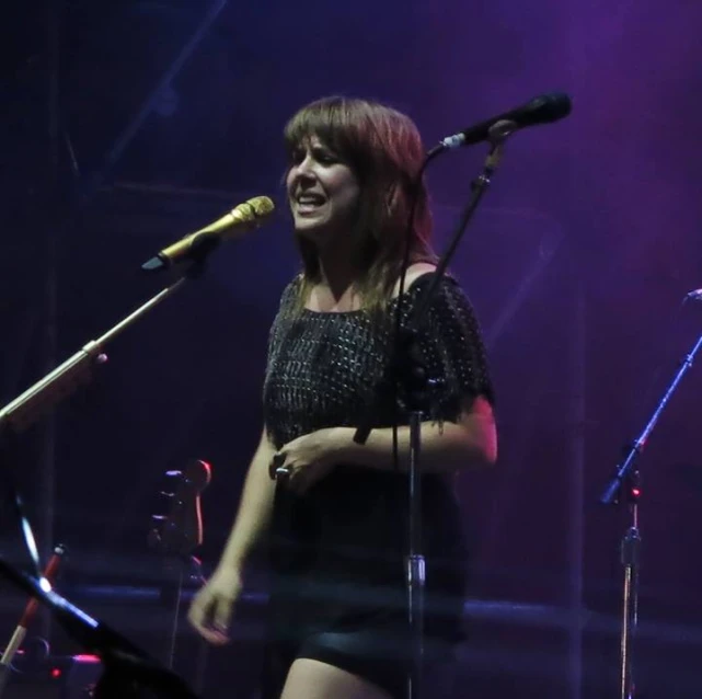 a woman in an all - black dress standing next to a microphone