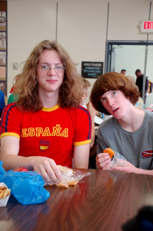 a couple of people sitting at a wooden table eating food