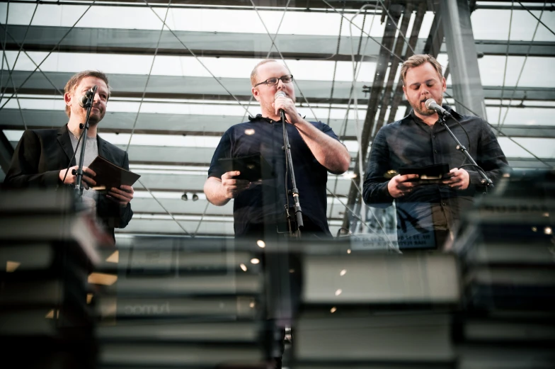 a group of men stand outside of a building, some using cellphones and microphones