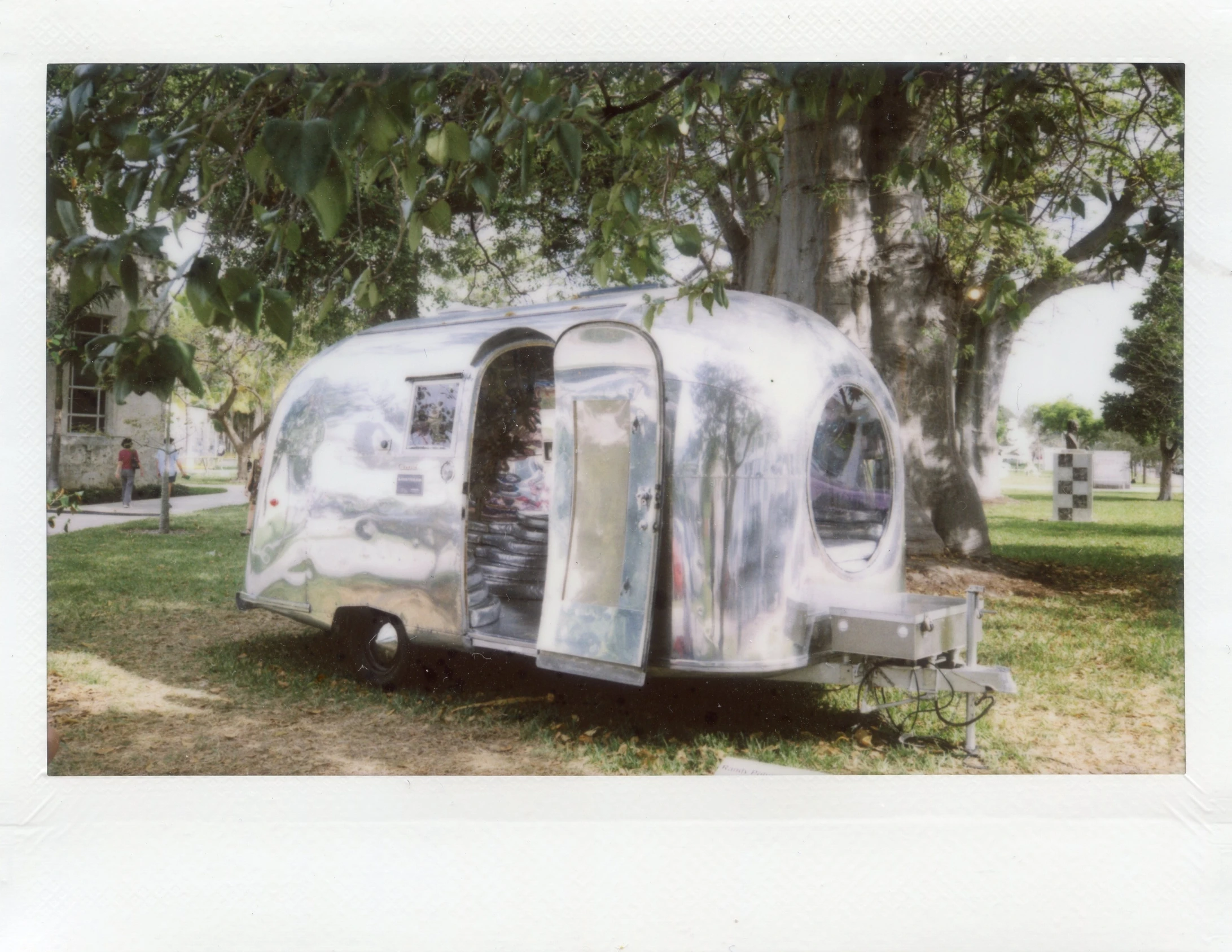 an old camper parked near a tree and in the grass