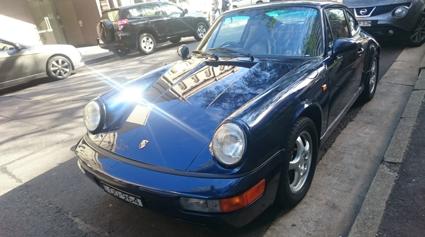 a blue porsche car on the sidewalk and another cars parked on the sidewalk behind it