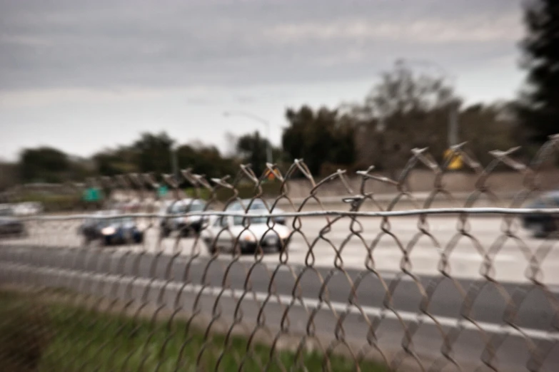 a close up view of cars driving on the road and behind a barbed wire fence