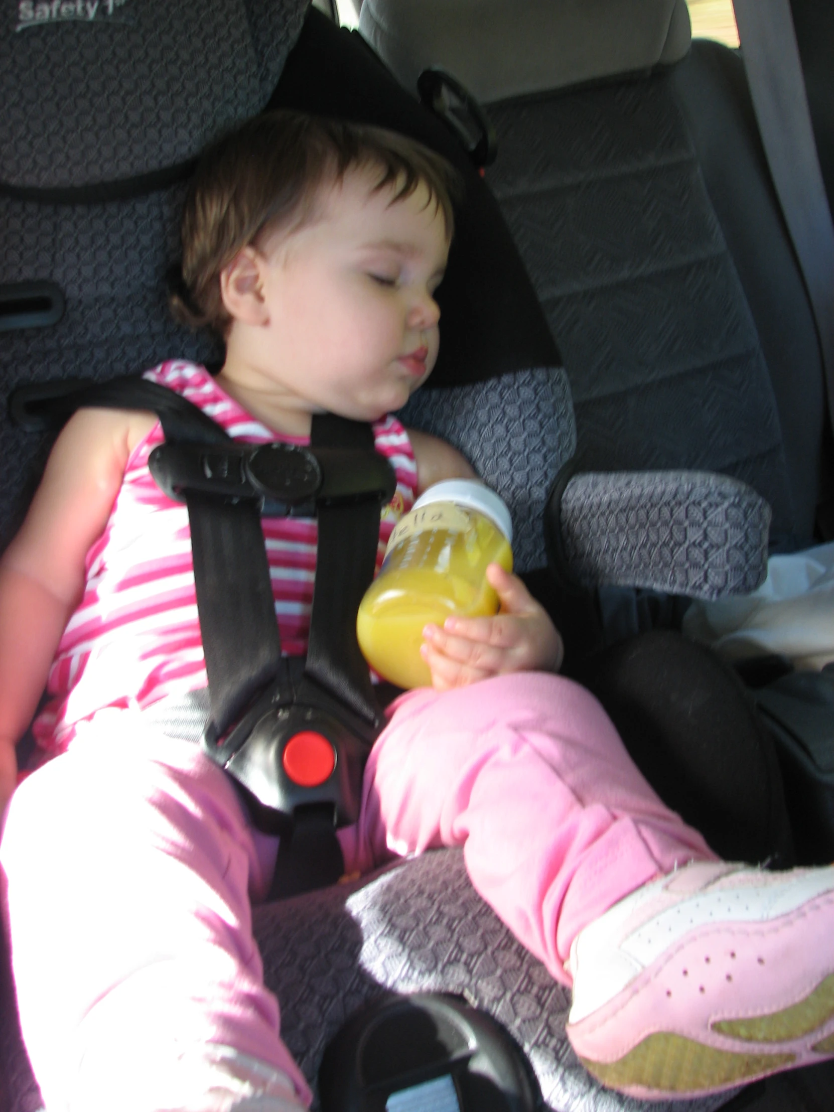 a young child drinks from a bottle while sitting in a car seat