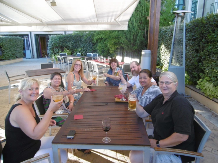 people are smiling at the table while holding wine glasses