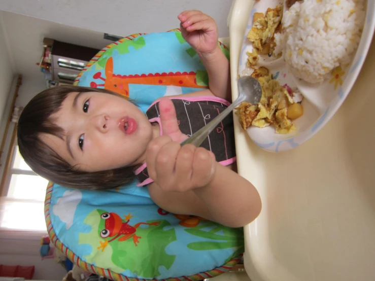 little girl eating with spoon from plate on table