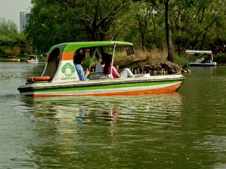 people on a green and orange boat traveling on water