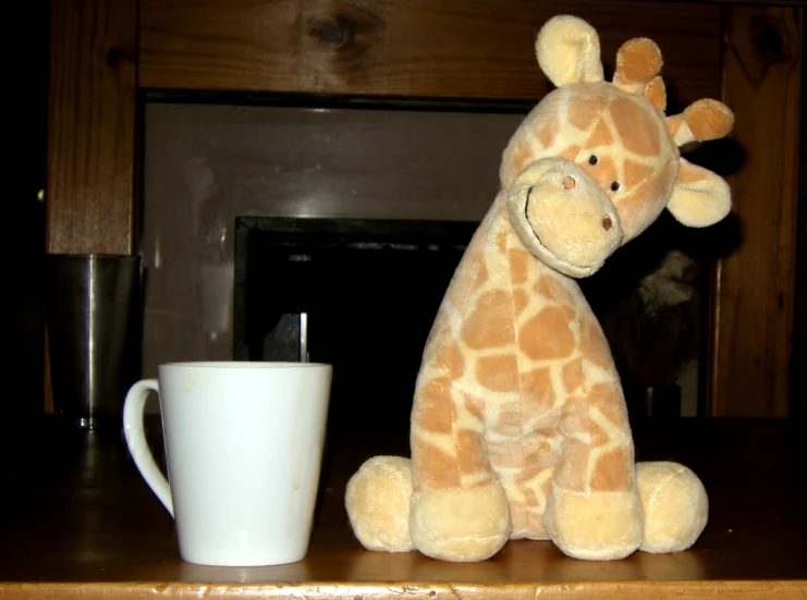 a very cute small giraffe sitting by a cup