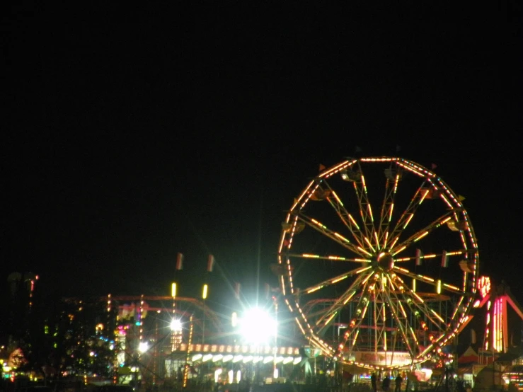 a ferris wheel is lit up at night, in the distance