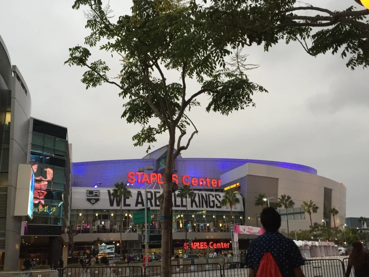 people are standing on the sidewalk in front of a stadium