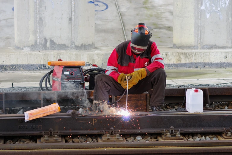 a worker with welding gear is on the train tracks