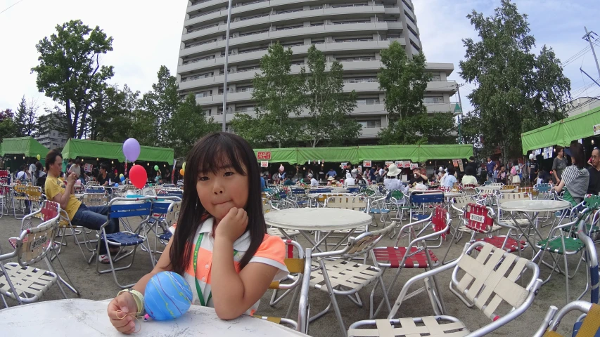 the little girl is sitting at a table outside with several chairs