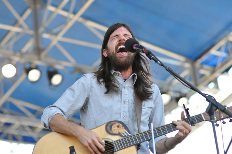 a man with long hair is singing while holding an acoustic guitar