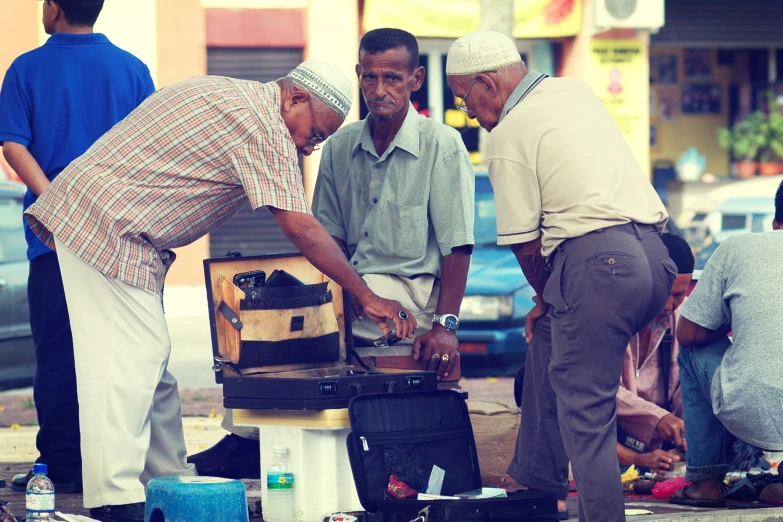 four men standing on a sidewalk looking at a suitcase