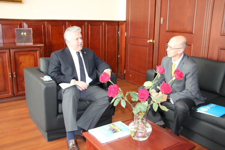 two older men sitting in black couches talking with each other