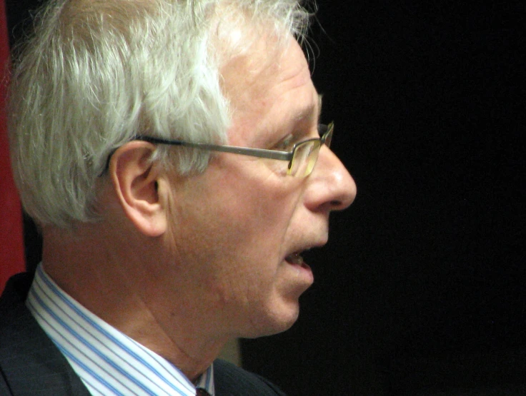 a man with gray hair and glasses on a black background