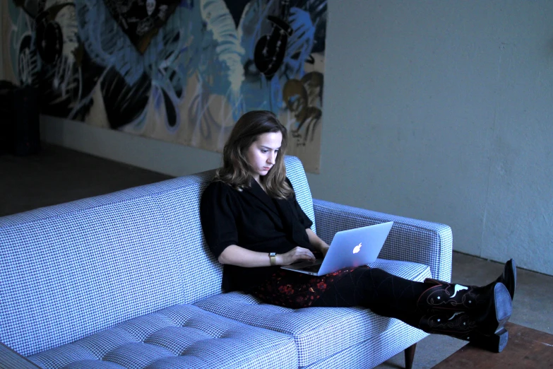 a woman sits on a couch using her laptop
