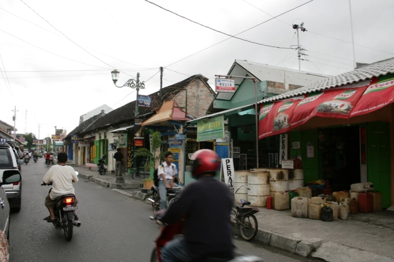 two people riding motorcycles down the road next to buildings