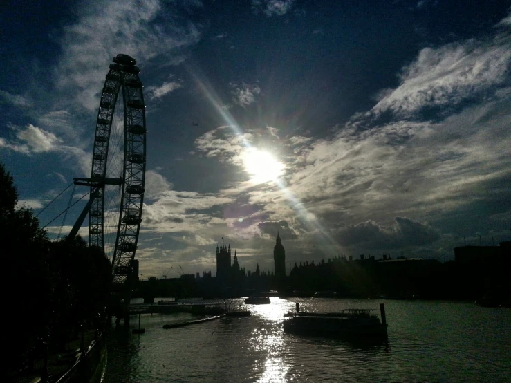 the sun is shining over the river with a ferris wheel