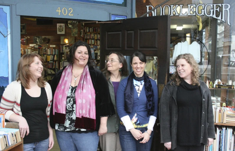 four women are standing outside a bookstore and laughing