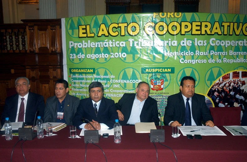 some men sitting at a table with a sign behind them