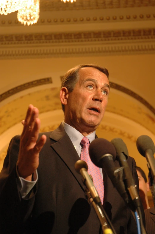 a man wearing a suit and tie speaking from a microphone