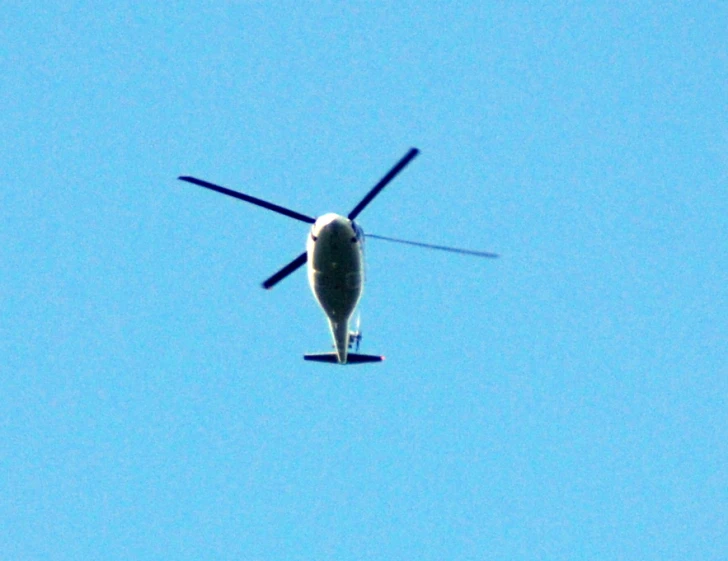 a single propeller helicopter in flight with a clear blue sky in the background