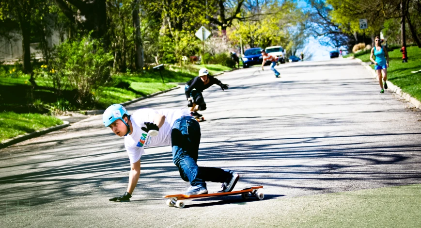 boys skateboarding down a street next to trees