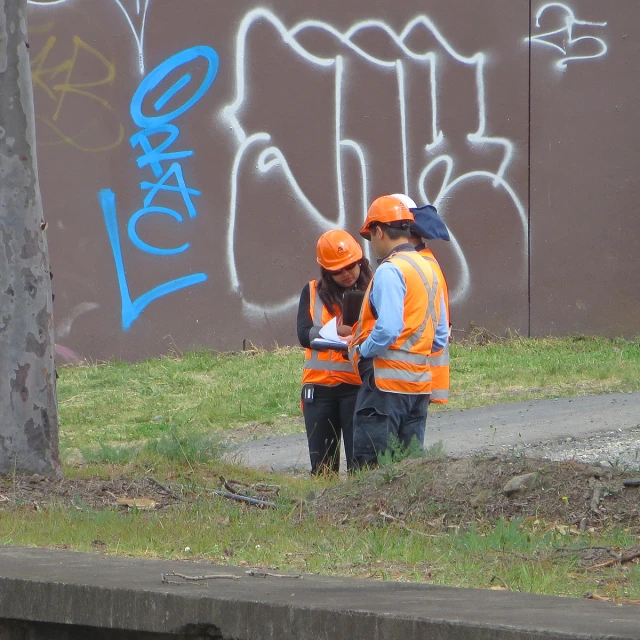 two construction workers are standing on the sidewalk next to a graffiti covered wall