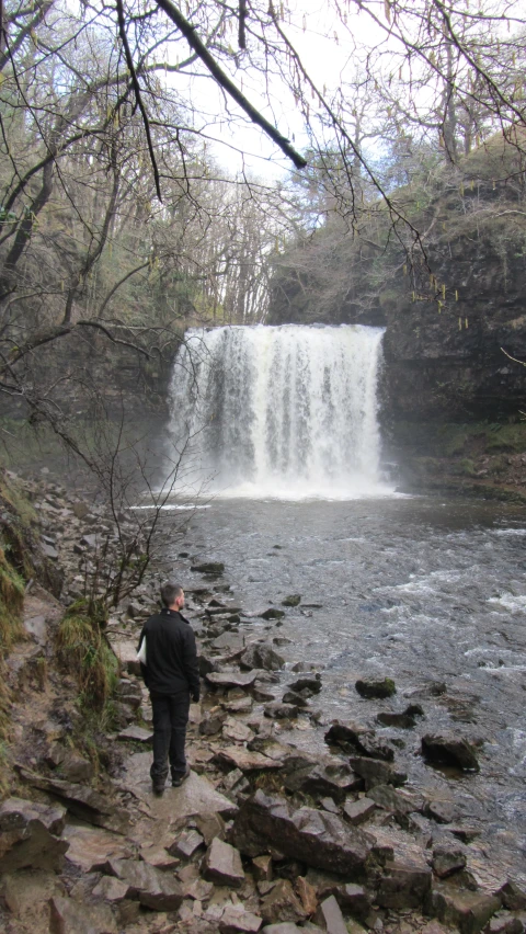 a person standing by a waterfall looking up at it